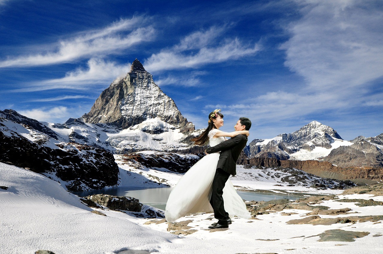 Unique souvnir from a honeymoon, photoshopped pictures as a creative gift. A couple in wedding dresses against the Alps.